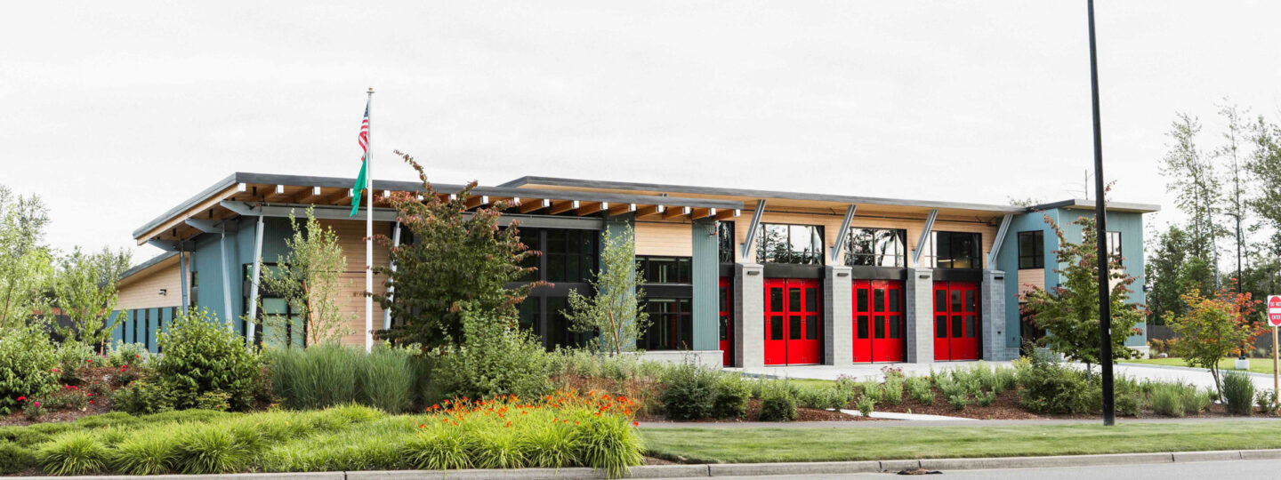 Exterior view of East Pierce Fire & Rescue’s Station 117 in Tehaleh. The modern fire station features a row of bright red bay doors, tall windows, and a clean concrete apron, with an American flag and Washington State flag visible to the left.