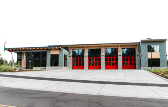 Exterior view of East Pierce Fire & Rescue’s Station 117 in Tehaleh. The modern fire station features a row of bright red bay doors, tall windows, and a clean concrete apron, with an American flag and Washington State flag visible to the left.
