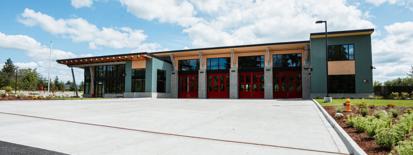 Exterior view of East Pierce Fire & Rescue’s Station 117 in Tehaleh. The modern fire station features a row of bright red bay doors, tall windows, and a clean concrete apron, with an American flag and Washington State flag visible to the left.